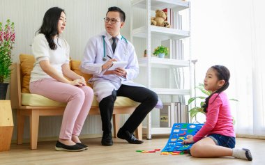 Asyalı doktor hasta geçmişi hakkında notlar yazarken aynı zamanda küçük etnik bir kızın annesiyle hastaneye gelip gitmediğini kontrol ediyor.