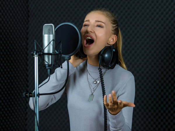 Young female singer performing song near microphone in professional recording studio with soundproof wall