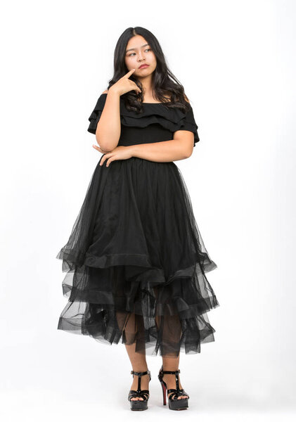 Портрет в полный рост снимает милую улыбающуюся молодую девушку-подростка в красивом черном платье, поднимающую руку и смотрящую в камеру на изолированном белом фоне студии. Младшая девочка танцует со счастьем