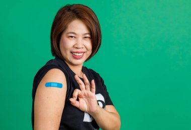 Orta yaşlı Asyalı bir kadının stüdyo fotoğrafı. Gülümseyin. Tamam el işareti ve mavi alçı bandajlar omuz hizasında..