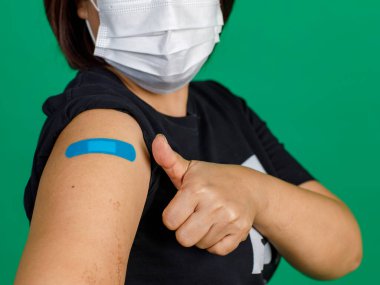 Kadın hastanın yüz maskesi taktığı yakın çekim stüdyosu yeşil arka plandaki doktordan Coronavirus covid 19 aşısı aldıktan sonra başparmağının sargı bezi ile sarıldığını gösteren kameraya bakın..