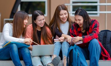 Bir grup Asyalı kız öğrenci merdivenlerde oturmuş üniversitede tatildeyken akıllı telefondan komik videolar izliyorlar. Gençlerin özel hayat arkadaşı konsepti.