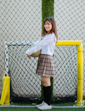 Etekli genç Asyalı kız öğrenci futbol sahasında duruyor ve kameraya bakıyor.