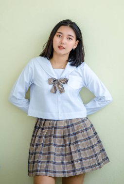 Üniversite binasının bej duvarının yanında durmuş kameraya bakan sakin Asyalı kız öğrencinin portresi.