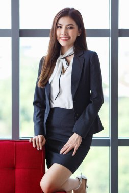 Ofisteki kanepede uzanmış kameraya bakan zarif giysiler giymiş gülümseyen Asyalı kadın girişimci ya da sekreter portresi