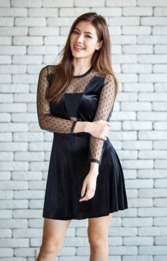 Beyaz tuğla bir duvarın arkasında duran siyah elbiseli, genç ve sevimli Asyalı bir kadının portresi. Dostça bir duruş ve sıcak bir his..