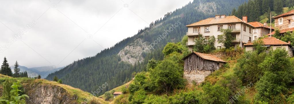 Village houses and outbuildings in coniferous forest on the steep slopes of the Rhodope Mountains in cloudy weather