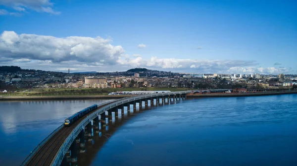 Kuş bakışı bir kum tepesi. Dundee, İskoçya - 01 Mart 2021 Yolcu treni, İskoçya 'nın Dundee şehrinin arka planında bulunan Tay Nehri üzerindeki köprüde seyahat ediyor..