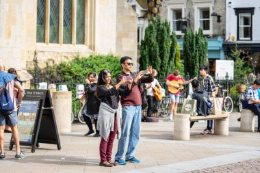 Cambridge, İngiltere, 1 Ağustos 2019. Kings Koleji önünde güneşli bir günde Cambridge caddesinde yürüyen ve fotoğraf çeken turistler