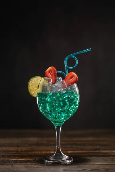 Un cocktail de couleur émeraude dans un verre à glace décoré de citron vert et de fraises avec une paille bouclée — Photo