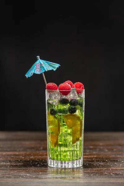 Зеленый коктейль в высоком бокале, украшенном апельсином, малиной и черникой — стоковое фото