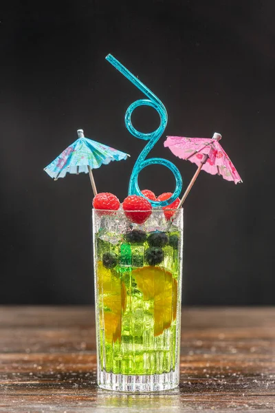 Зеленый коктейль в высоком бокале, украшенном апельсином, малиной и черникой — стоковое фото