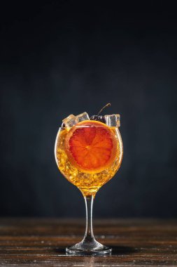 Sarı kokteyl ve bir bardak kiraz, bir dilim greyfurtla süslenmiş ahşap bir masanın üzerinde duruyor.