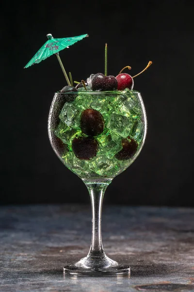Зеленый коктейль со льдом и вишней в стакане, украшенном зонтиками — стоковое фото