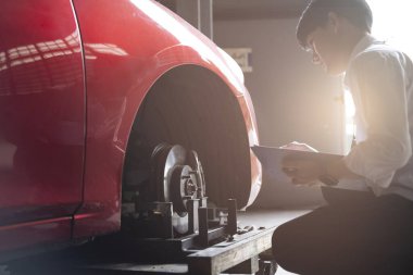 Asyalı satıcı müfettişi galeri arabasındaki tamirci garajında pano degistirme çarklarini kontrol ediyor ve yeni yil 2021 'e mutlu bir seyahat için sigorta yaptırıyor.