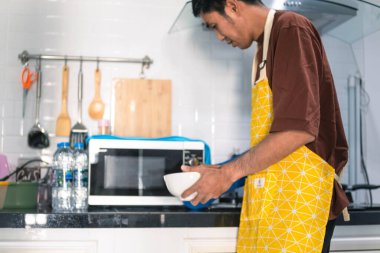 Bulanık Asyalı adam mutfağın mutfağında yemek pişiriyor. Mutfaktaki mikrodalgada harika ellere kâse ve spatula tutuyor. Arka planı bulanıklaştırıyor.