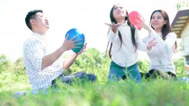 Genç aile parkta oturuyor ve balonlarla oynuyorlar.