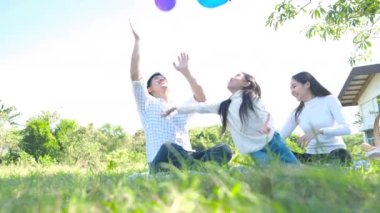 Genç aile parkta oturuyor ve balonlarla oynuyorlar.