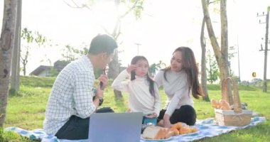 Gitarla çalan ve piknik sırasında parkta şarkı söyleyen sevimli Asyalı aile.