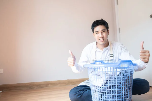 Asian man husband working homework.He is preparing clothes in basket to wash to washing machine for service lifestyle family togetherness in home