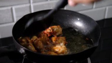 Asyalı bir adam mutfağında kızarmış tavuk pişiriyor. Elinde spatula ve tava var. Tayland yemeğiyle kızaran gaz sobasıyla. 