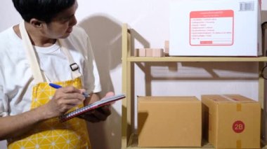 Yeni Normol Cvid-19 ile günlerce müşterilere kargo ya da mal taşımak için not defterine not almak üzere müşteri aramalarından sipariş veren Asyalı bir adam.
