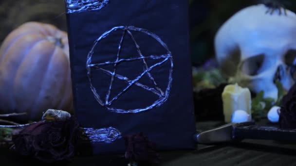 聚焦变化和平稳的相机运动 一本带有五芒星和人头的黑色书的特写 在万圣节前夕举行宗教仪式的女巫餐桌的概念 — 图库视频影像