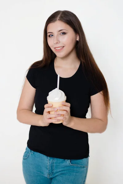 一个穿着黑色T恤和蓝色牛仔裤的年轻貌美的姑娘手里拿着一只手里拿着稻草的杯子 白色背景的工作室照片 — 图库照片