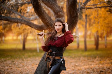 Portrait of an attractive slender woman with a saber on her shoulder against the background of an autumn park. clipart