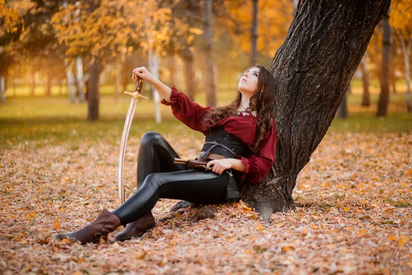 Piękna Młoda Kobieta Szablą Pistoletem Ręku Siedzi Przy Drzewie Jesiennym — Zdjęcie stockowe