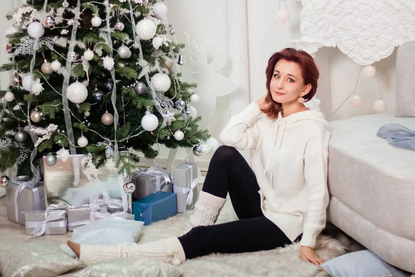 若い女性が毛皮の毛布の上にクリスマスツリーの下に座って 夢のようなポーズで — ストック写真