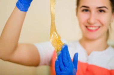 Bir tüy dökücü ustasının ellerinde sıvı şeker macununun yakın plan çekimi. Şekerli ellere odaklan, arkaplanda bulanık bir yüz.