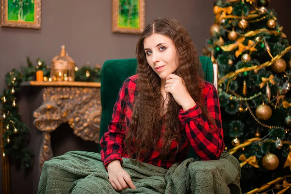 クリスマスツリーと暖炉を背景に 若い女性が遊びに包まれて座っています — ストック写真