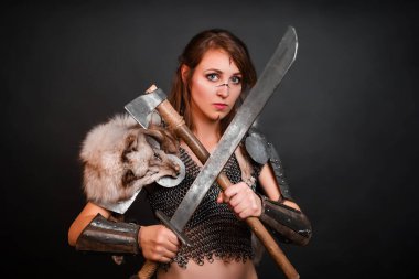 Zincirli zırhlı, zırhlı, omuzlarında zırhlı, omuzlarında kutup tilkisi kürkü olan barbar kadın savaşçı elinde bir balta ve elinde kılıçla karanlık bir arka planda duruyor..
