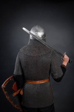 Zincirli zırhlı bir şövalye ve karanlık bir arka planda omzunda kılıç olan bir miğfer. Zırhlı Ortaçağ savaşçısı arkasında duruyor..