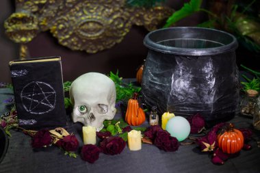 Masada pentagram, kafatası ve kazan bulunan kara kaplı bir defter ve cadılık malzemeleri. Cadılar Bayramı cadı sunağı kavramı.