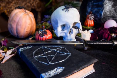 Üzerinde pentagram olan siyah bir kitaba odaklan. Siyah bir masanın üzerinde duran bir kafatası ve balkabağı. Cadılar Bayramı sihirli ritüel kavramı.