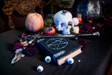 Üzerinde pentagram olan siyah bir kitaba odaklan. Siyah bir masanın üzerinde duran bir kafatası ve balkabağı. Cadılar Bayramı sihirli ritüel kavramı.