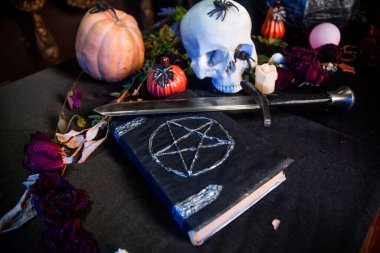 Üzerinde pentagram olan siyah bir kitaba odaklan. Siyah bir masanın üzerinde duran bir kafatası ve balkabağı. Cadılar Bayramı sihirli ritüel kavramı.