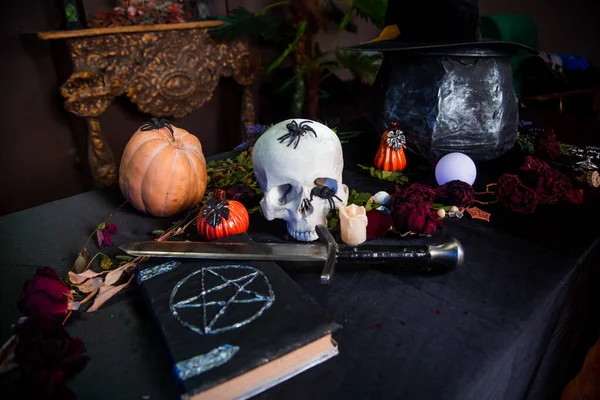 Bir insan kafatası, pentagram, balkabağı ve otlarla dolu bir kitabın yanındaki masada yatıyor. Sihirli ayin için sunak konsepti, Cadılar Bayramı kutlaması.