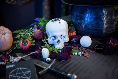 Masanın üzerinde büyücülük malzemeleriyle birlikte çok renkli gözleri olan bir insan kafatası yatıyor. Cadılar Bayramı cadı sunağı kavramı.
