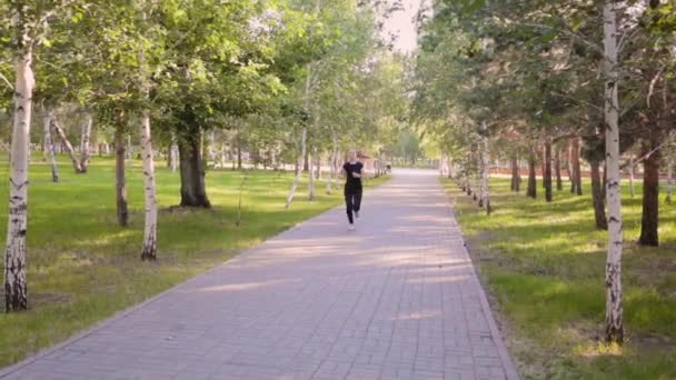 Μια Νεαρή Λεπτή Γυναίκα Τρέχει Στο Δρομάκι Ενός Καλοκαιρινού Πάρκου — Αρχείο Βίντεο