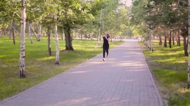 一个年轻纤细的女人沿着一个夏季公园的小巷跑着 户外运动与健康生活方式的概念 — 图库视频影像