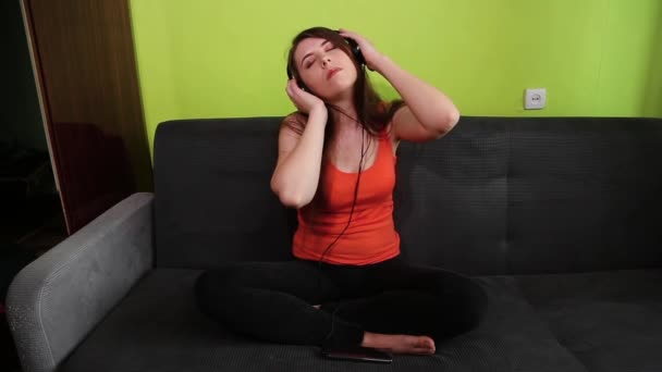 Una Chica Atractiva Sienta Una Posición Loto Sofá Con Auriculares — Vídeo de stock