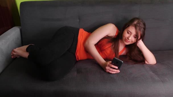 Uma Jovem Atraente Está Deitada Num Sofá Com Smartphone Nas — Vídeo de Stock