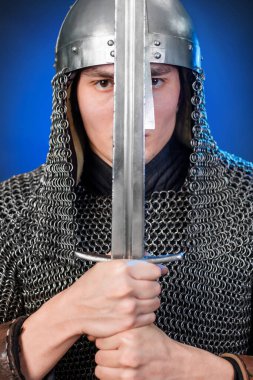 Viking döneminin ortaçağ savaşçısının portresi ve Haçlı Seferleri 'nin başlangıcı. Zincirli zırhlı ve miğferli şövalye koyu siyah ve mavi arka planda izole edilmiş bir kılıçla donatılmış..