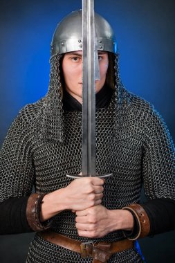 Viking döneminin ortaçağ savaşçısının portresi ve Haçlı Seferleri 'nin başlangıcı. Zincirli zırhlı ve miğferli şövalye koyu siyah ve mavi arka planda izole edilmiş bir kılıçla donatılmış..