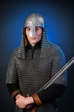 Viking döneminin ortaçağ savaşçısının portresi ve Haçlı Seferleri 'nin başlangıcı. Zincirli zırhlı ve miğferli şövalye koyu siyah ve mavi arka planda izole edilmiş bir kılıçla donatılmış..