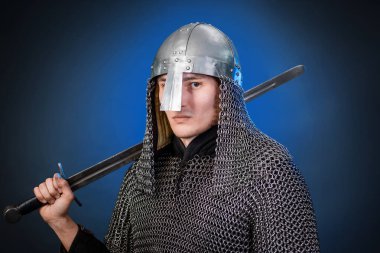 Viking döneminin ortaçağ savaşçısının portresi ve Haçlı Seferleri 'nin başlangıcı. Zincirli zırhlı ve miğferli şövalye koyu siyah ve mavi arka planda izole edilmiş bir kılıçla donatılmış..