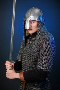 Viking döneminin ortaçağ savaşçısının portresi ve Haçlı Seferleri 'nin başlangıcı. Zincirli zırhlı ve miğferli şövalye koyu siyah ve mavi arka planda izole edilmiş bir kılıçla donatılmış..